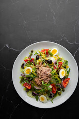 French salad Nicoise with tuna, egg, green beans, tomatoes, olives, lettuce, onions and anchovies on a gray background. Healthy food