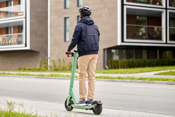 transport, safety and people and concept - young man in helmet riding electric scooter on city street