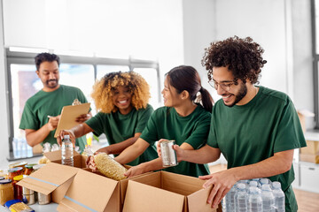 charity, donation and volunteering concept - international group of happy smiling volunteers packing food in boxes according to list on clipboard at distribution or refugee assistance center