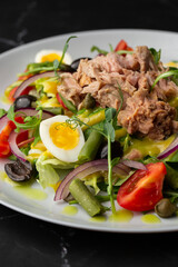 French salad Nicoise with tuna, egg, green beans, tomatoes, olives, lettuce, onions and anchovies on a gray background. Healthy food