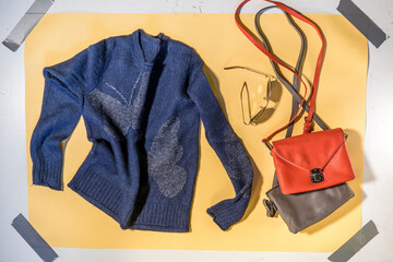 blue women's sweater and two handbags on yellow background flat lay