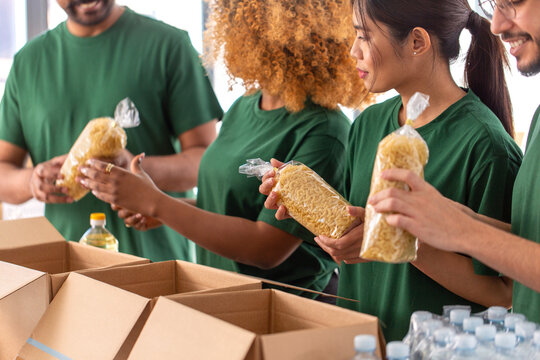 charity, donation and volunteering concept - close up of international group of happy smiling volunteers packing food in boxes at distribution or refugee assistance center
