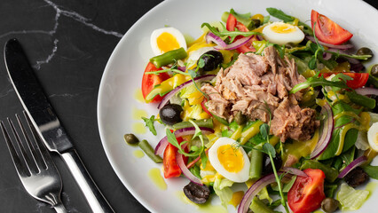French salad Nicoise with tuna, egg, green beans, tomatoes, olives, lettuce, onions and anchovies on a gray background. Healthy food