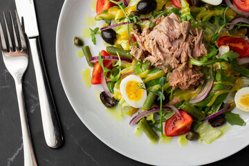 French salad Nicoise with tuna, egg, green beans, tomatoes, olives, lettuce, onions and anchovies on a gray background. Healthy food