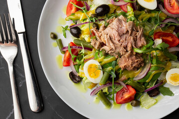 French salad Nicoise with tuna, egg, green beans, tomatoes, olives, lettuce, onions and anchovies on a gray background. Healthy food