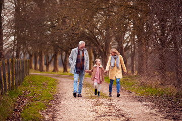 Fototapeta premium Grandparents With Granddaughter Outside Walking Through Winter Countryside Holding Hands