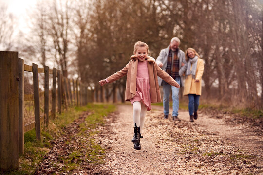 Grandparents With Granddaughter Outside Walking Through Winter Countryside