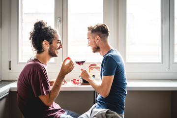 two lovers having a snack in the kitchen, gay married gay couple drinking red wine and eating vegetables indoor, LGBT people lifestyle