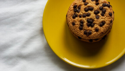 Pile of chocolate chip cookies on a yellow plate and on a white tablecloth