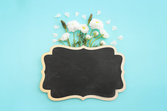 Top view image of white flowers composition and empty blackboard over blue pastel background