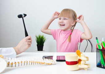 A little cheerful 5-year-old girl laughs in the neurologist's office and looks at the neurological hammer. Examination of children by a pediatric neurologist