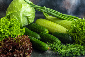 Fresh vegetables for salad. Tomatoes and lettuce, cucumbers with zucchini and cabbage with dill. Spring harvest, benefits and vitamins. On a dark background.