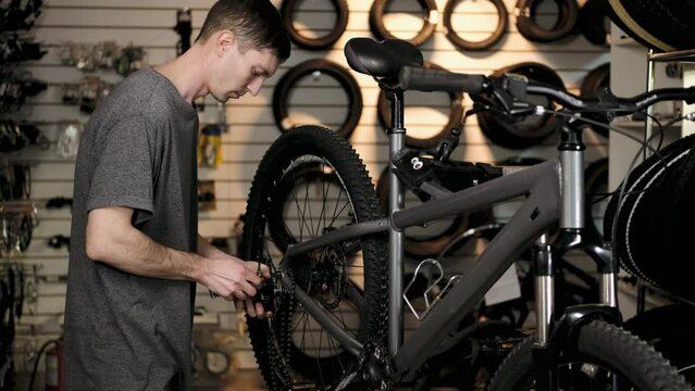Bicycle repair.  young mechanic repairs bicycle after trip. man twists gears with keys and pulls chain. Repair service for sports and mountain bikes. Repair of broken frame
