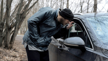 Homeless man walks up to someone else's car, male burglar robber looks through the slightly open...