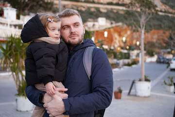 Obraz premium Handsome bearded caucasian blond man,father holding,hugging baby girl in street.Love,happy parent,dad and daughter,child