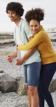 Vertical video of happy biracial couple embracing on seaside
