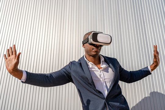 Businessman wearing virtual reality simulator standing with arms outstretched in front of wall on sunny day