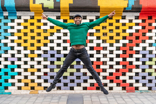 Happy man with arms outstretched jumping in front of multi colored wall