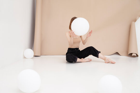Young woman catching white balloon sitting against brown backdrop