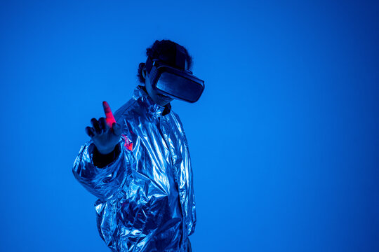 Woman wearing virtual reality simulator gesturing by standing against blue background