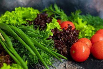 Fresh vegetables for salad. Tomatoes and lettuce, cucumbers with zucchini and cabbage with dill. Spring harvest, benefits and vitamins. On a dark background.