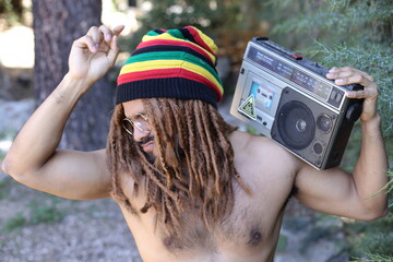 Attractive man with dreadlocks listening to music on stereo cassette player