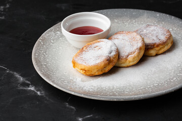 Cottage cheese pancakes, Syrniki or Cheesecakes with red sauce isolated on black marble background. Homemade food. Tasty breakfast. Selective focus.