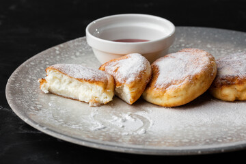 Cottage cheese pancakes, Syrniki or Cheesecakes with red sauce isolated on black marble background. Homemade food. Tasty breakfast. Selective focus.