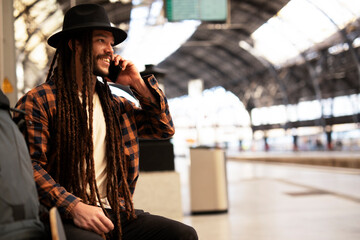 Fototapeta premium Handsome guy at railway station waiting for the train. Young man waiting to board a train. Urban guy using the phone..