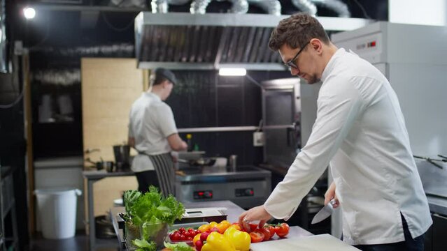 Chef taking restaurant order slip, telling something to sous chef and then starting food preparation at kitchen table