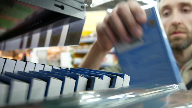 Close-up of many chocolate bars in a row on a store shelf and a man takes one
