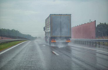 Semi-trailer truck driving on the highway with other cars during heavy rain in summer, wet road....