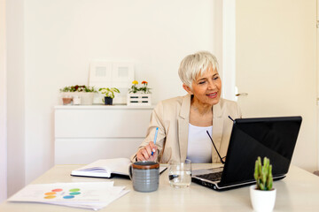 Shot of a mature woman working on a laptop at home. Mature woman working from her home office. Multitasking of mature business female entrepreneur working from home office.