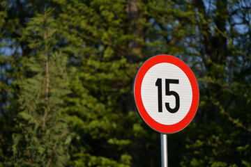 Traffic sign indicator showing the maximum speed limit at 15 kmh photographed against forest background. Slow speed announcement. Transportation industry.