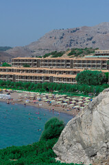 Kolymbia beach with sun loungers and hotels on the background of a mountainous area with green vegetation (Rhodes, Greece)