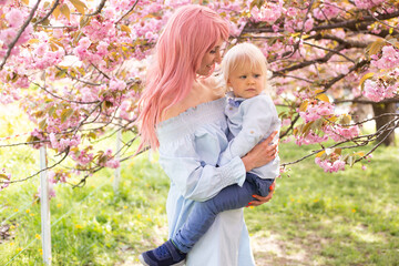 happy woman with a child in her arms happy. Sakura blossom in spring Park. Joy of motherhood and child development. Cherry blossom tree in late spring