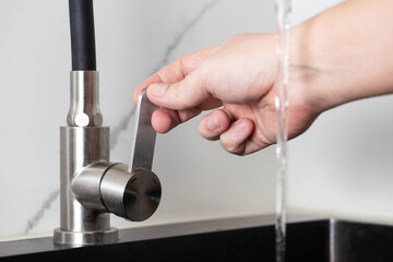 A man's hand regulates the power of the jet from a water tap. Cold and hot water, close-up. Quality...