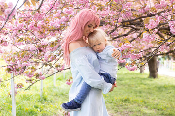 Mother with little son in the park walk near the sakura tree