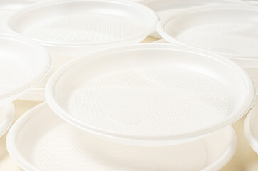 Disposable white plastic tableware on a beige background. The concept of nature pollution