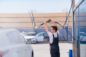 self-service car wash. a man in a work jumpsuit washes the car from a hose. 