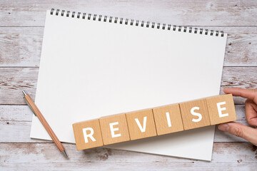 修正・改訂のイメージ｜「REVISE」と書かれた積み木、ノート、ペン、手