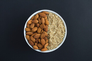 Dried whole and chopped almond in the white bowl on the black background. Top view. Closeup.