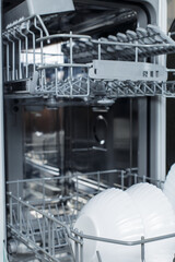 Well-washed dishes in the dishwasher. Built-in dishwasher with white plates in front. dishwasher concept