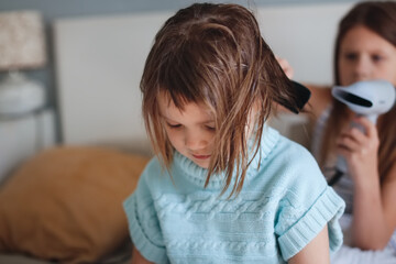 Little sister blow-drying her little sister's hair. Children in the bedroom on the bed, siblings take care of each other