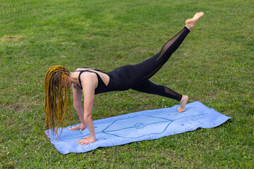 Woman yogi with dreadlocks stretching doing practicing phalankasana plank pose push ups press ups variation on yoga mat. Relaxing in the morning. Fitness instructor coach showing exercises 