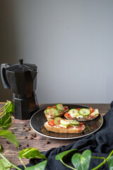 fresh and healthy sandwiches on black plate and wooden table next to the black coffee maker and a plant on grey background