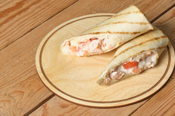 cut roll with chicken on tray on a wooden background, copy space, stuffing in pita bread, fast food concept