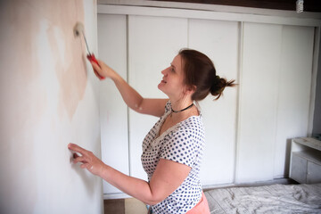 Woman paints a wall in a room with a roller, do-it-yourself repair