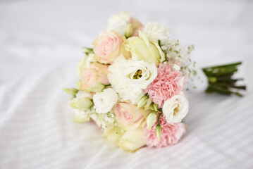 Beautiful flowers bouquet lying on white sheets. Pink, white, ivory roses as a wedding present. Festive decorations for holiday. Symbolism and wedding traditions.