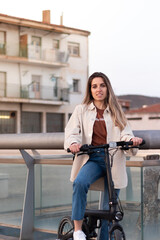 Fototapeta na wymiar Vertical portrait of young woman looking at camera holding an electric bicycle in an urban enviroment